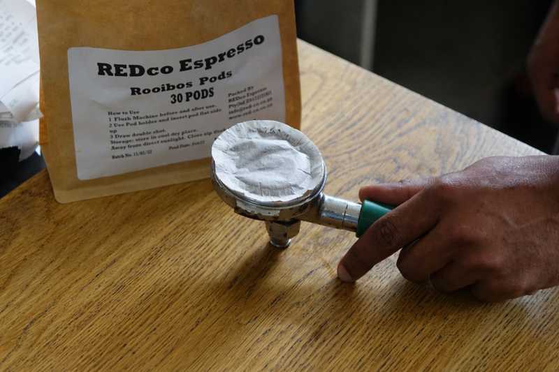 Padträger mit eingelegtem Rooibos Pad vor einer REDco-Espresso-Packung im Café