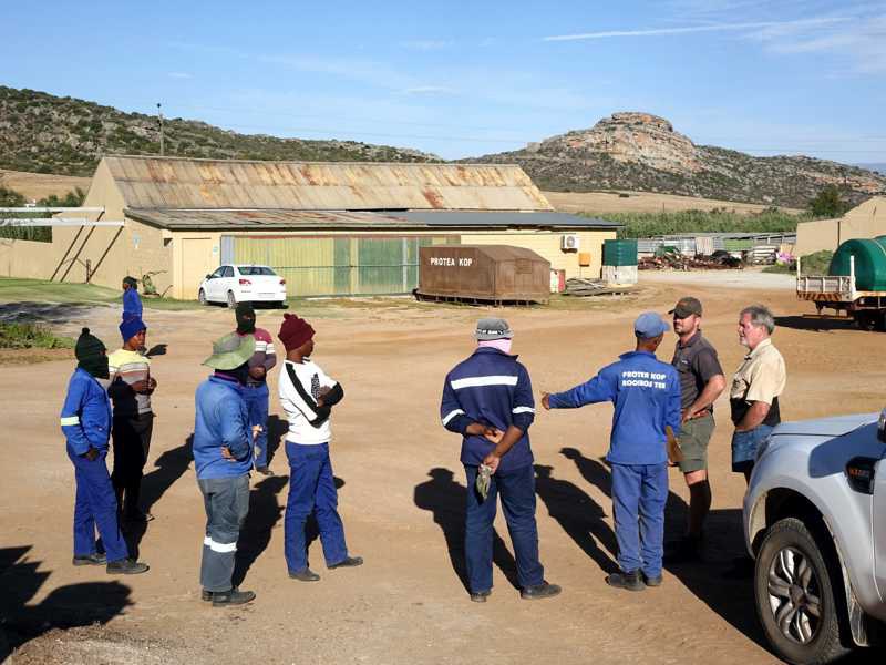 Short team briefing in the yard: staff standing in a circle in front of farm buildings