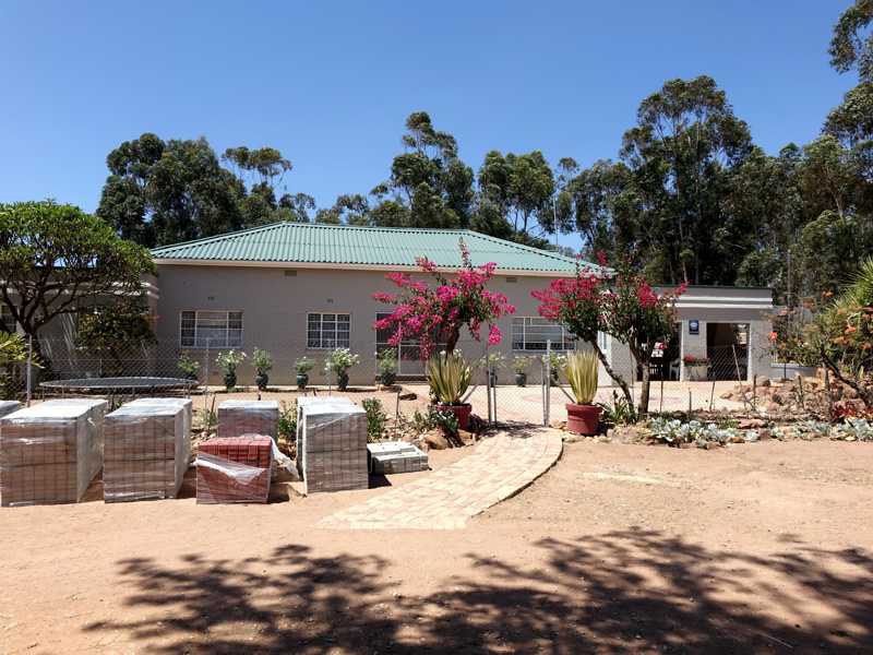Farmhouse of Meerlandsvlei Farm with garden, path and building materials in the foreground under a blue sky.