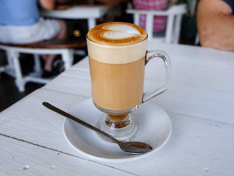 Creamy rooibos milk drink with milk foam in a glass on a light café table