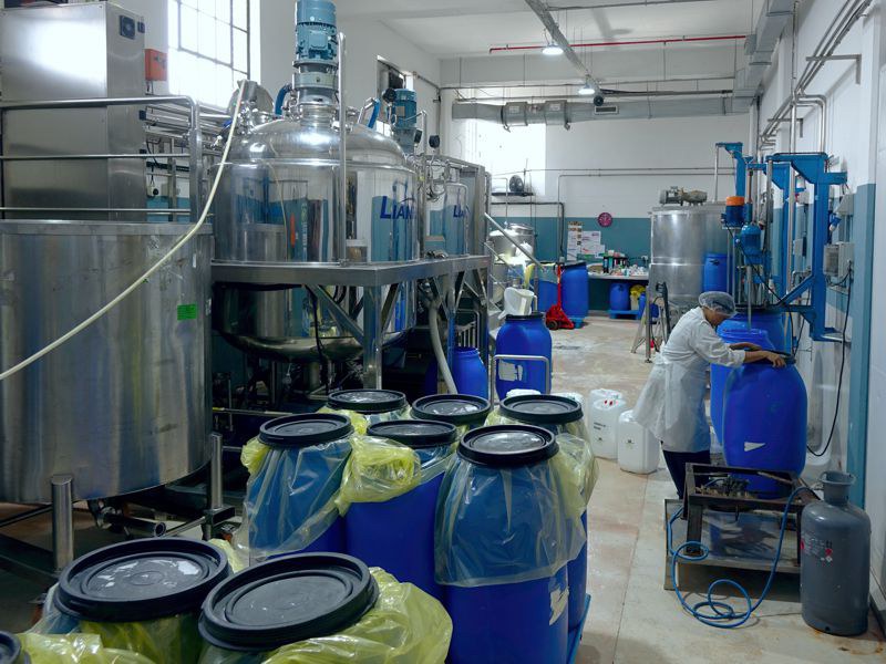 Salle de mélange chez African Extracts avec de grands réservoirs en inox, des fûts bleus et une employée.