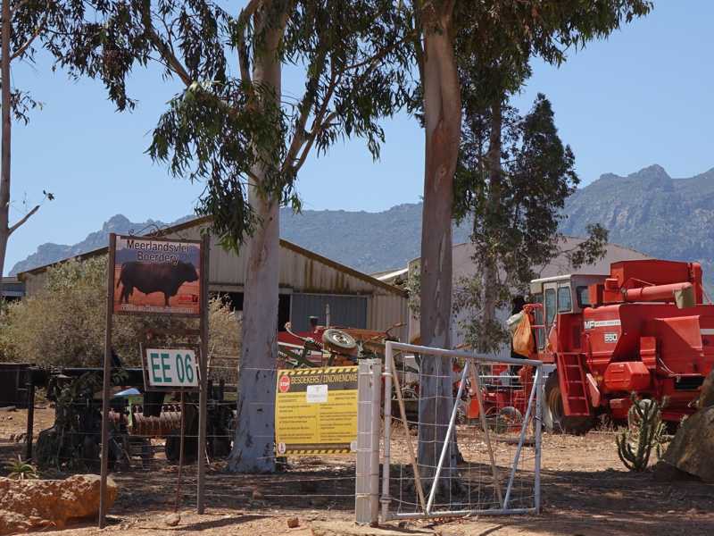 Entrée de la ferme Meerlandsvlei avec panneau, portail et machines agricoles, montagnes en arrière-plan.